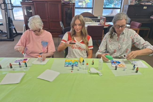 Three women sit at a table working on an alcohol ink art project. 