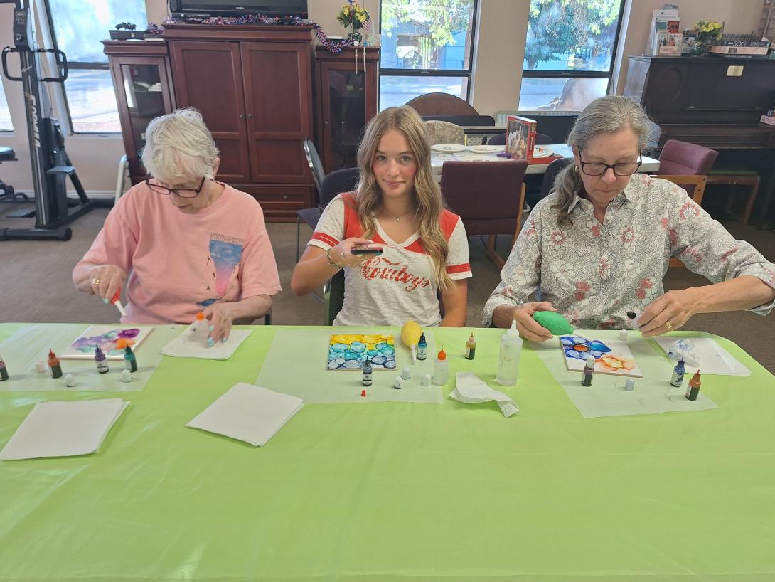 Three women sit at a table working on an alcohol ink art project. 